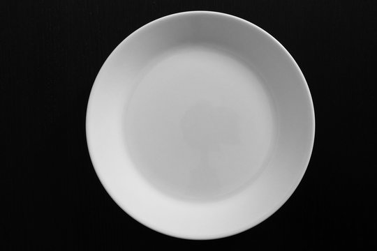 Empty white plate on black wooden table