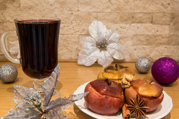 Red mulled wine and baked apples with melting honey, nuts and spices, cinnamon and anise. Decorated with  christmas decoration, silver and violet balls, brick wall background.