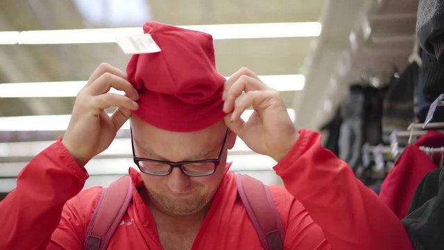 Close-up shot of a bald man trying on a new red winter hat in shop.