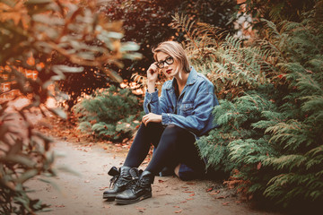 beautiful young girl in jacket and glasses sitting on a gorund in a park. Fall season time scene. Hipster trends clothes style