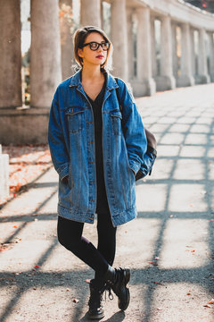 Beautiful redhead girl in glasses and jacket walking at alley with columns. Autumn season time.