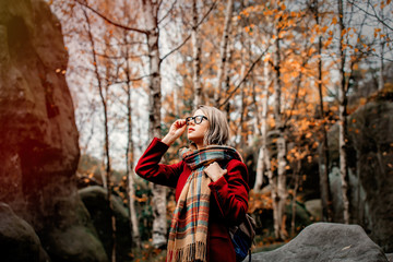 Beautiful young girl in scarf and coat in a forest with rocks. Autumn season time in mountains