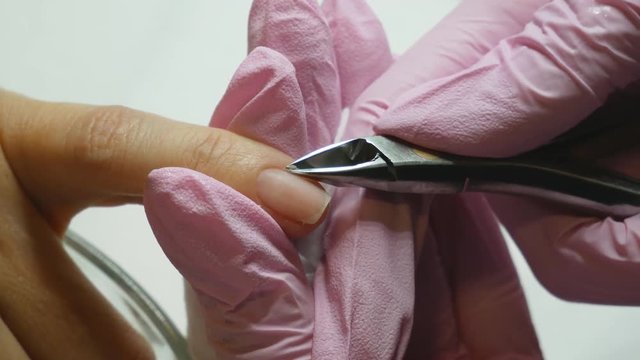 Manicurist cleaning nails to female client. Nail beautician in protective gloves removing cuticles with metal instrument