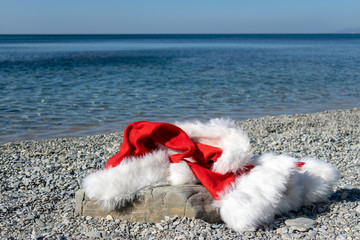 Santa Claus clothing and hat lies on a large stone on the seashore. Santa went swimming
