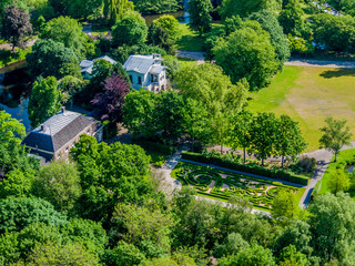 Aerial view of houses surrounded by leafy trees with green foliage, decorative gardens, areas with green and yellow grass, sunny day in Rotterdam city, South Holland in the Netherlands