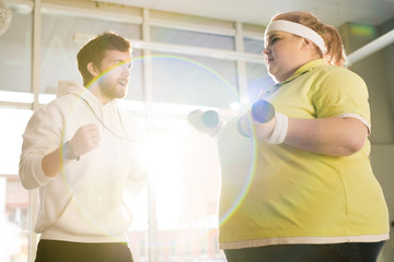 Waist up portrait of fat young woman working out with dumbbells during weight loss training with...