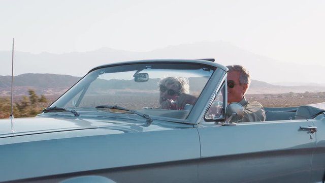 Smiling senior couple driving classic convertible on highway