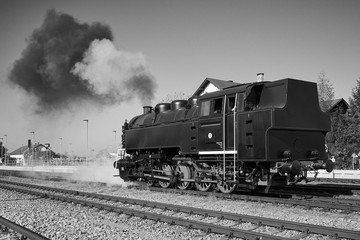 Retro steam train locomotive in the vilage railway station making smoke and steam and waiting on the track to be connected with railway carriage, black and white picture