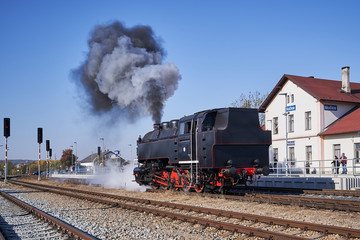 Fototapeta na wymiar Retro steam train locomotive in the vilage railway station Nucice in Czech Republic making smoke and steam and waiting on the track to be connected with railway carriage.