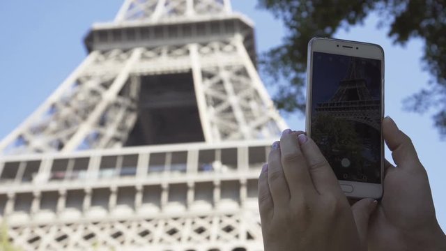 Crop back view of woman using smartphone and taking shot of Eiffel Tower in sunlight