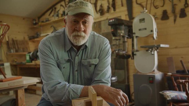 Portrait of confident carpenter leaning on shaving horse in workshop / Spring City, Utah, United States