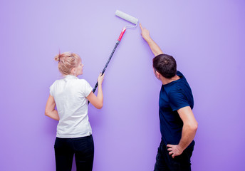 wife and husband paint the wall with a roller in purple in their new home.
