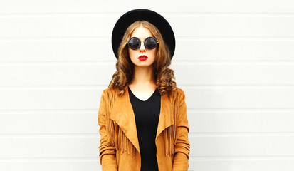 Fashion woman in black round hat, sunglasses, jacket on gray wall background