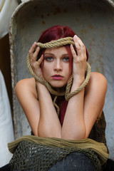 A red headed beauty poses for the camera with a  melancholic expression on her face. She is tied ...
