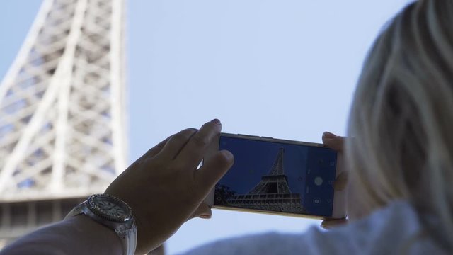Crop view in closeup of woman using phone and taking photo of Eiffel Tower in sunlight