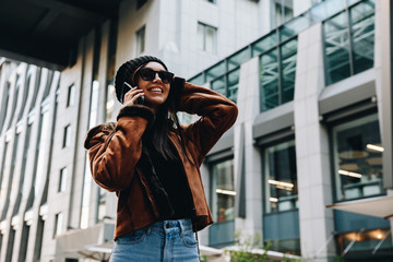 City style. Technology. Autumn/spring. Stylish girl in casual clothes is talking on the mobile phone and smiling while walking outdoors