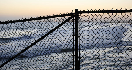 Fototapeta premium Background plate of Silhouetted chain-link fence in front of a California beach