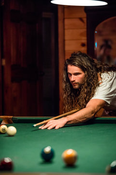 Young man concentrates as he hits a pool ball across the table