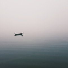 Fototapeta na wymiar Mistic lonely boat in the middle of the lake, mist fog