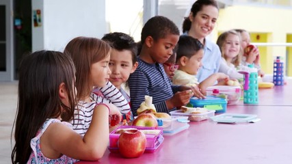 Elementary school kids and teacher at a table eating lunch - Powered by Adobe