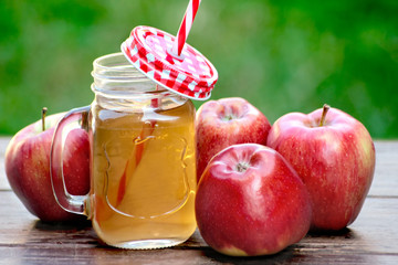 Glass of apple juice and red apples on wooden background      