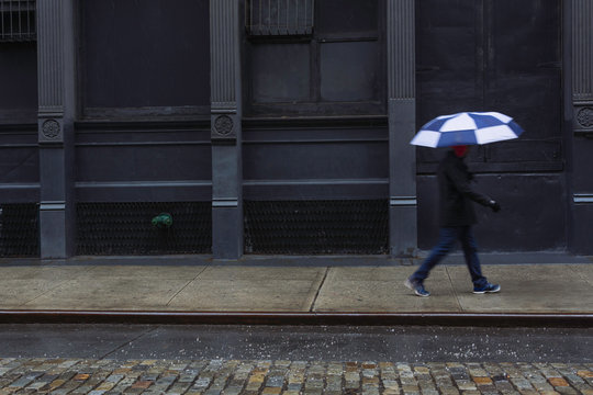 Man With Umbrella Walking Along Street Through Winter Sleet Storm