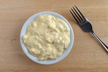 Top close view of a portion of potato and egg salad in a small bowl with a fork to the side on a wood table.