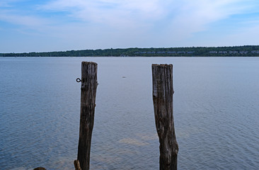 The ruins of an old pier in the water with two posts at Stockton Harbor in Maine with a blue sky above and a distant sailboat.