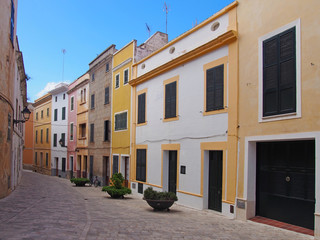 Fototapeta na wymiar a scenic view of an empty street of bright painted yellow traditional houses in ciutadella menorca with bright blue summer sky