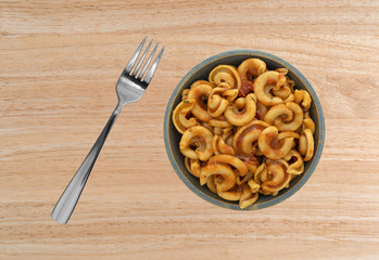 Overhead view of cold pasta with tomato chunks and seasonings with olive oil in an old stoneware...
