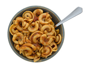 Overhead view of cold pasta with tomato chunks and seasonings with olive oil in an old stoneware bowl with a fork in the food isolated on a white background.