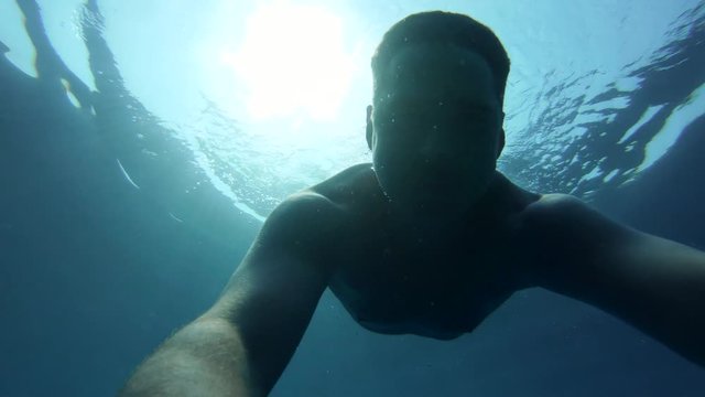 Young man is snorkeling under the clear water - sea. He is smiling end enjoying vacation on a warm sunny day. Underwater Gopro selfie.