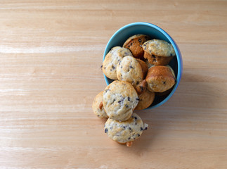 Several freshly baked bite size blueberry muffins a blue bowl on its side spilling onto a wood...