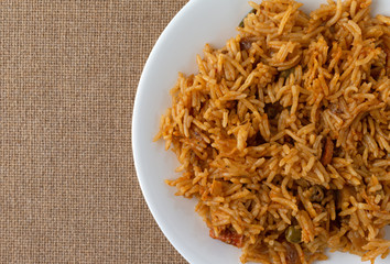 Top close view of a serving of spicy vegetable rice on a white plate atop a brown tablecloth illuminated with window light.