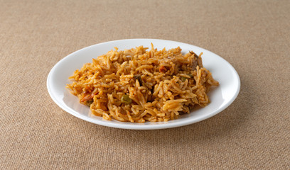 A serving of spicy vegetable rice on a white plate atop a brown tablecloth illuminated with window light.