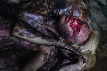 Couple of colorful shiny girls laying on the mirror floor one of them looking at camera