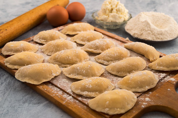 Fototapeta na wymiar Raw dumplings stuffed on a cutting Board, flour, cottage cheese, eggs.