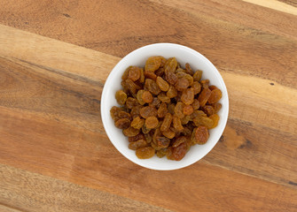 Top view of a small white bowl filled with golden raisins on a wood cutting board.