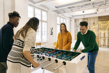 Four Co-Workers Playing Tabletop Soccer in Bright Office Foyer