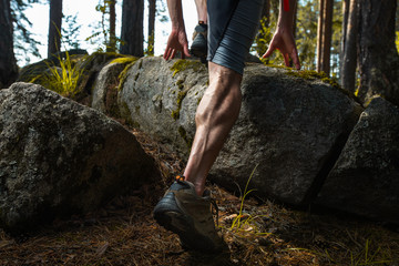 Muscled leg of the trail running athlete crossing rocky terrain in the summer forest