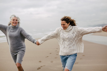 Active senior woman and her daughter enjoying on the beach in winter.