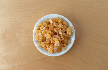 Top view of a small bowl filled with dried diced peaches on a birch plywood table top illuminated with window light.