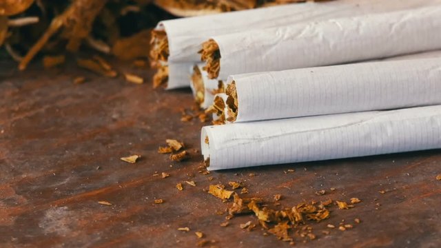Homemade cigarettes or roll-up stuffed with tobacco are on a table next to dry tobacco leaves