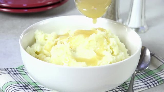 Pouring turkey gravy onto a bowl of mashed potatoes