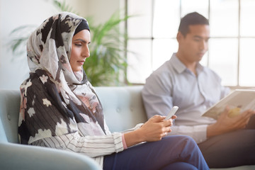 Woman in headscarf using mobile smartphone indoors