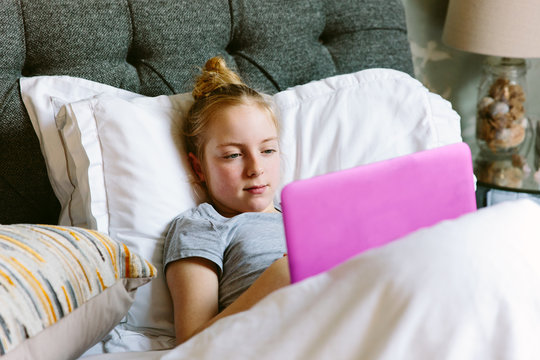 Preteen girl streaming a tv programme on her laptop in bed