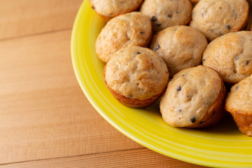 Side close view of freshly baked bite size chocolate chip muffins on a yellow plate atop a wood table.