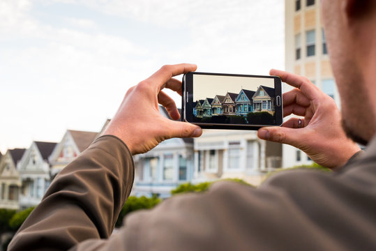 Man uses a smartphone to photograph a row of homes in San Franci