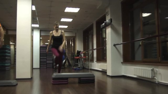 Fat funny man trying to do steps. Near young beautiful young sport woman actively doing step aerobics. camera moves to the left