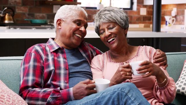 Smiling Senior Couple Relaxing With Hot Drink On Sofa At Home
